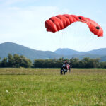 About Us closeup of a man parachuting near the ground with a red parachute during daylight
