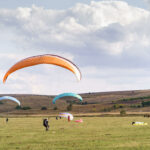 About Us paragliders flying under blue sky in a green field