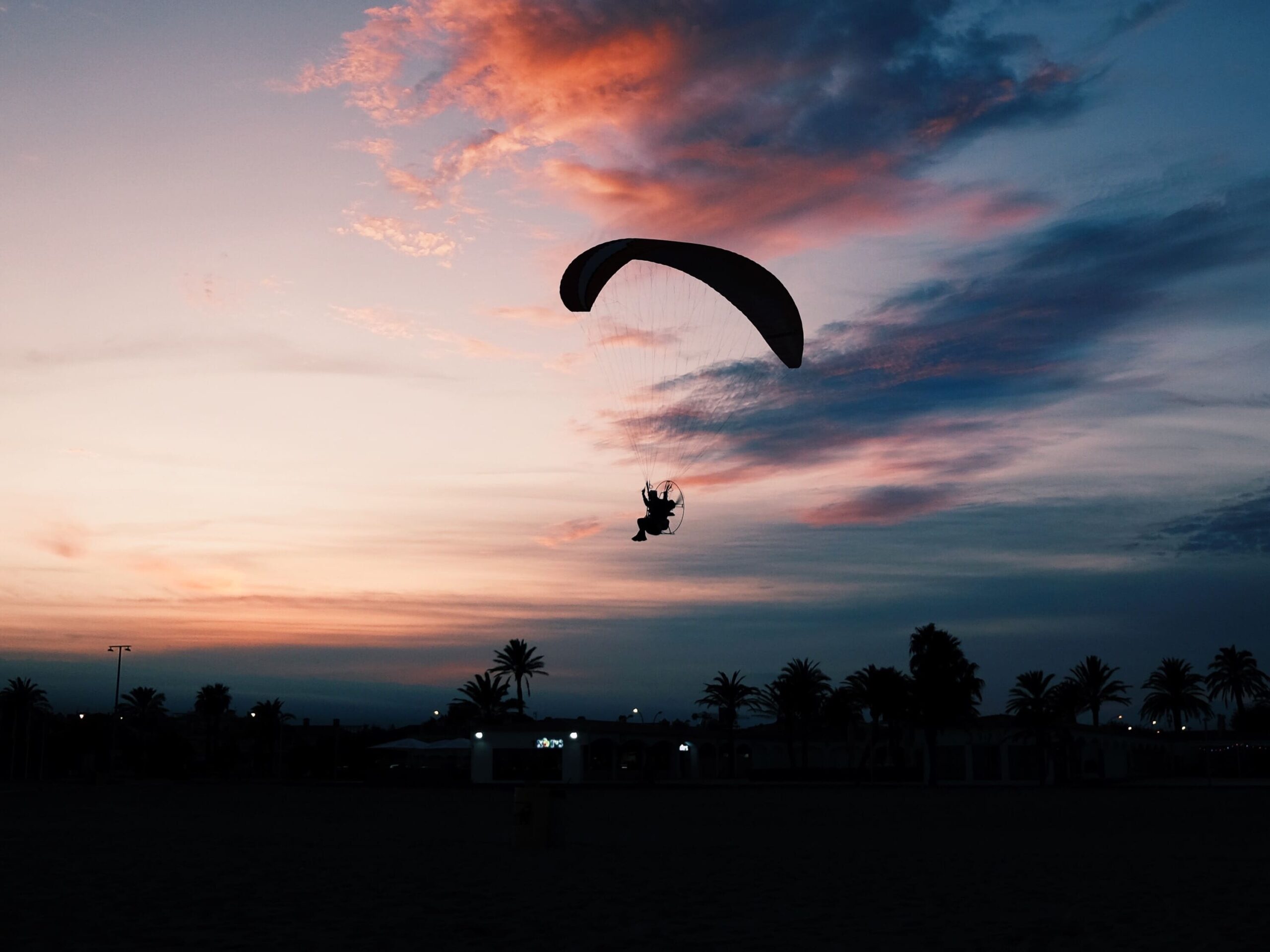 horizontal shot beach with person gliding down paramotor parachute